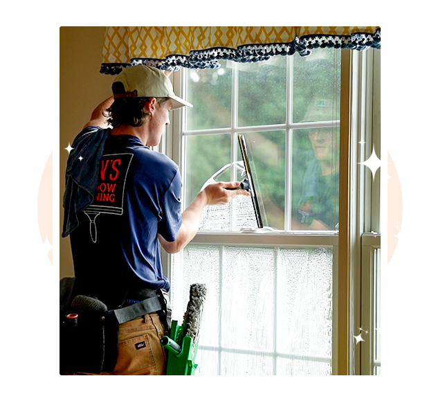 Professional window cleaner using squeegee on interior residential window — satisfaction guaranteed streak-free results in Malvern PA