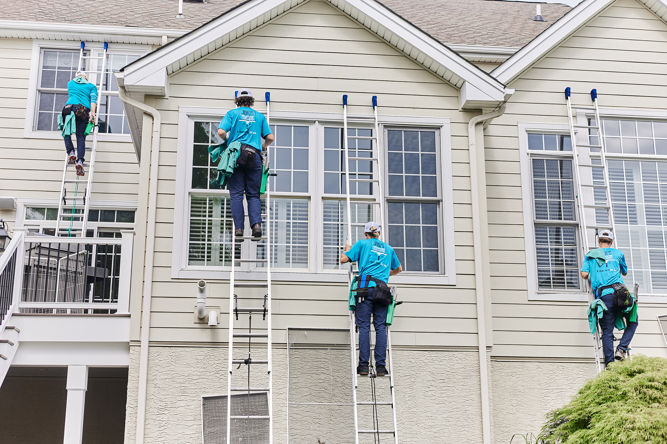 Residential window cleaning crew using ladders to professionally wash hard-to-reach second-story windows